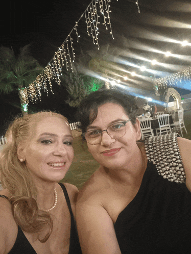 two women posing for a picture with a string of lights behind them