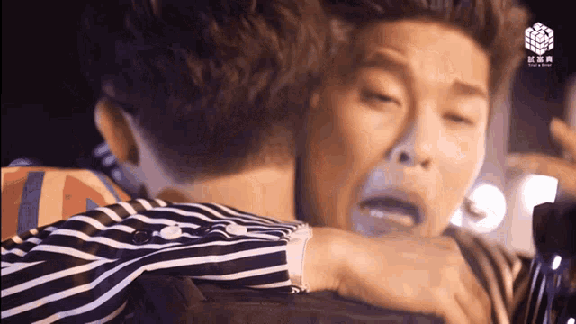 a man in a striped shirt is hugging another man with chinese writing on the bottom right
