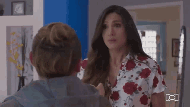 a woman in a floral shirt is talking to a boy in a room .