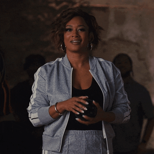 a woman in a grey jacket holds a black bowling ball