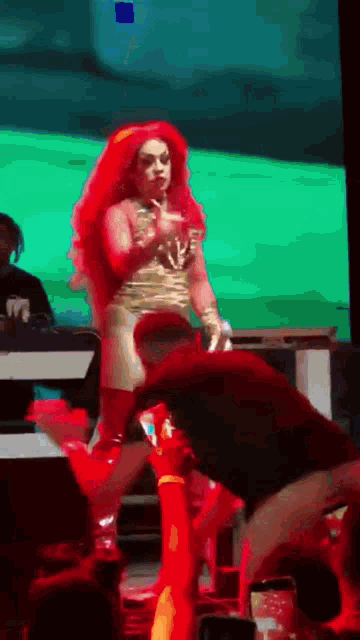 a drag queen with red hair is dancing on stage in front of a crowd