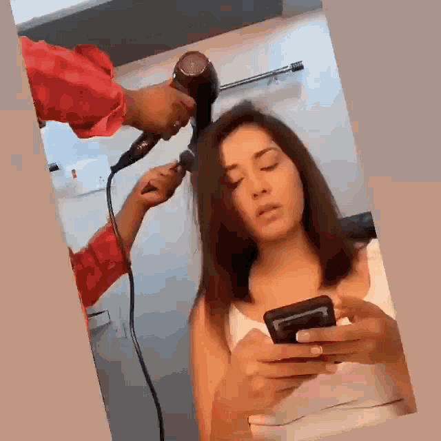 a woman is getting her hair blow dried while holding a phone