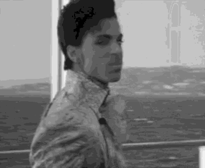 a black and white photo of a man standing on a balcony overlooking the ocean .