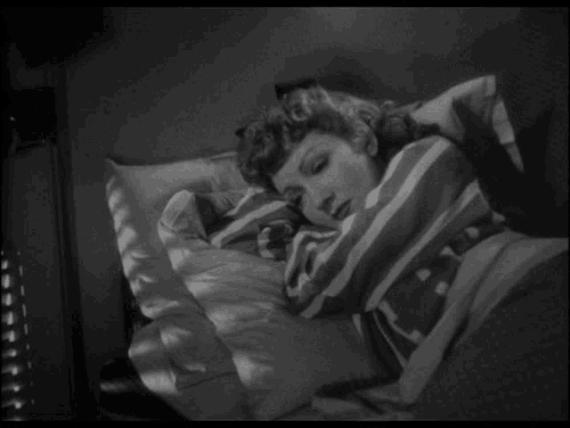a woman is laying in a bed with a striped blanket and pillows .
