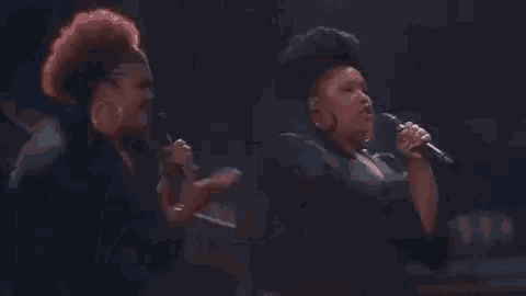 a woman is singing into a microphone while standing next to a man in a dark room .