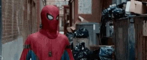 a man in a spiderman costume is standing in a alleyway surrounded by trash bags .