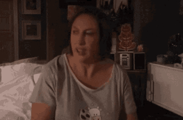 a woman in a gray shirt is sitting on a bed .