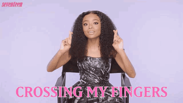 a woman in a black dress is sitting in a chair with the words crossing my fingers below her