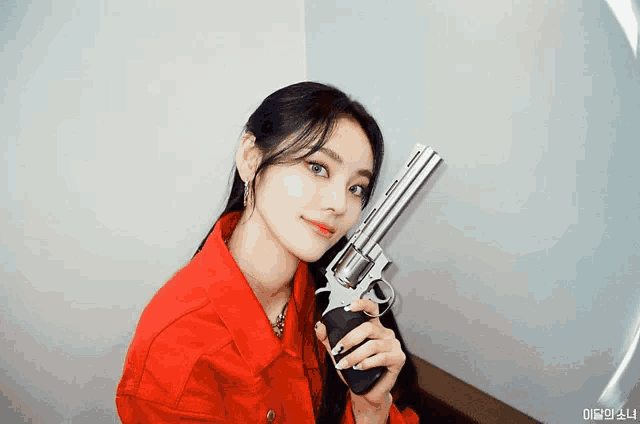 a woman in a red jacket holds a large gun