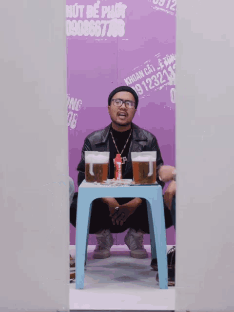 a man sits at a small table with two cups of beer and a can of coke