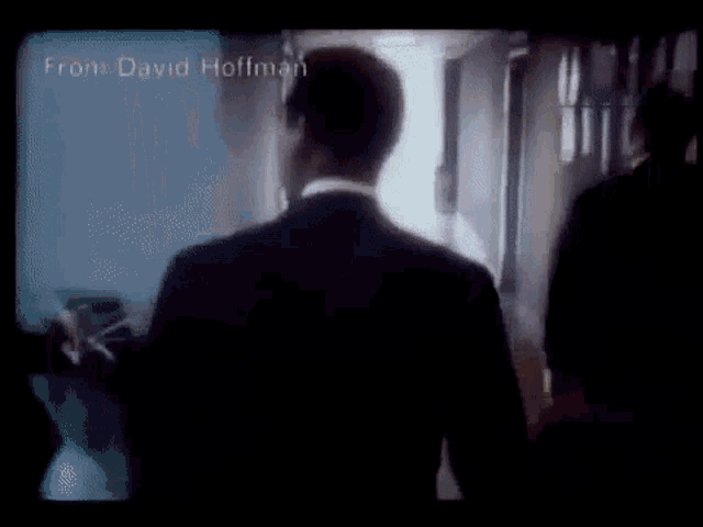 a man in a suit is walking down a hallway in a dark room in a movie .