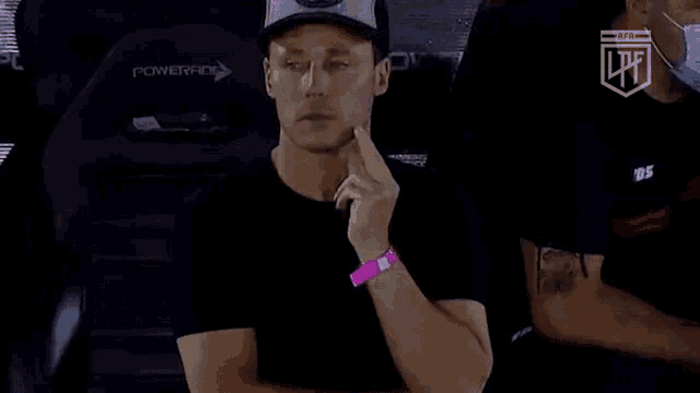 a man wearing a hat and a pink wristband is sitting in a stadium .