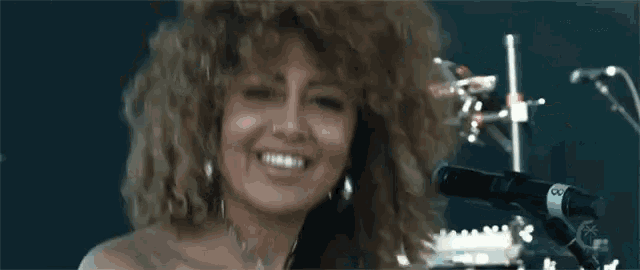 a woman with curly hair is smiling in front of a microphone with the letter g on it