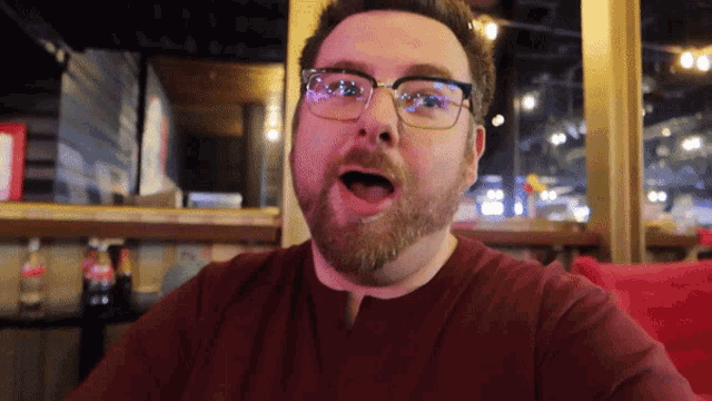 a man with glasses and a beard is sitting at a table with his mouth open