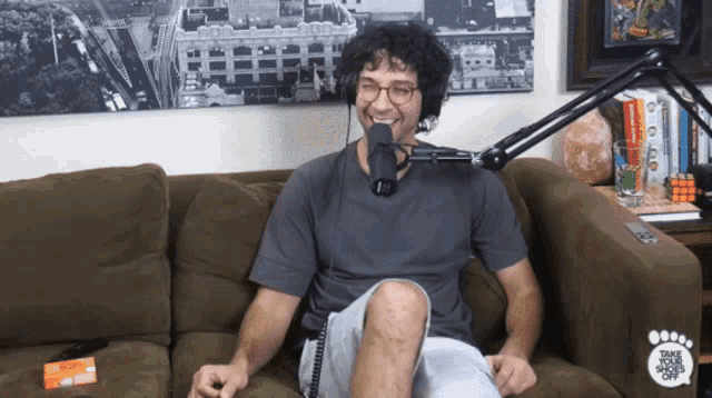 a man sitting on a couch talking into a microphone with the words take your shoes off