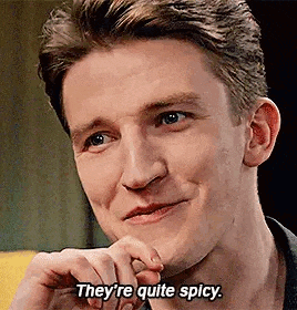 a man is smiling and saying `` they 're quite spicy '' while sitting on a couch .