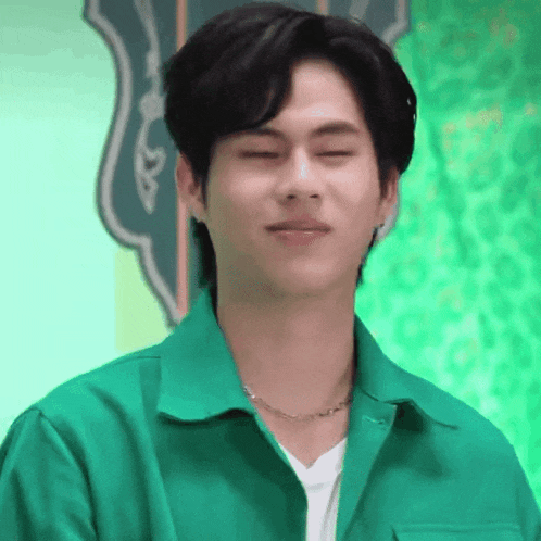 a young man wearing a green jacket and a necklace is making a funny face with his eyes closed .
