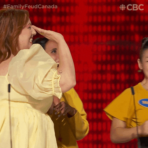 a woman in a yellow dress is laughing while another woman in a yellow shirt holds her nose