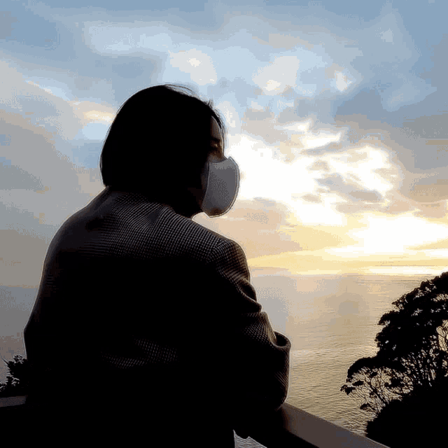 a woman wearing a face mask looks out over a body of water