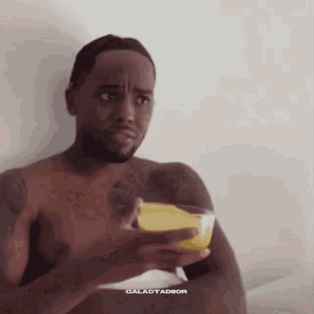 a shirtless man is holding a glass of orange juice and making a funny face .