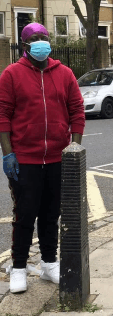 a man wearing a face mask and gloves is standing on a sidewalk