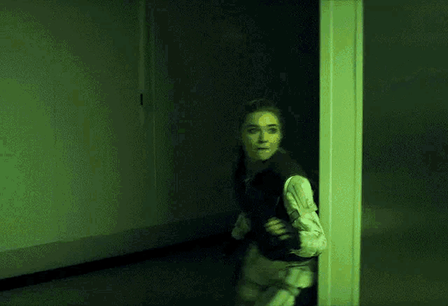 a woman is running through a dark hallway with a green light behind her .