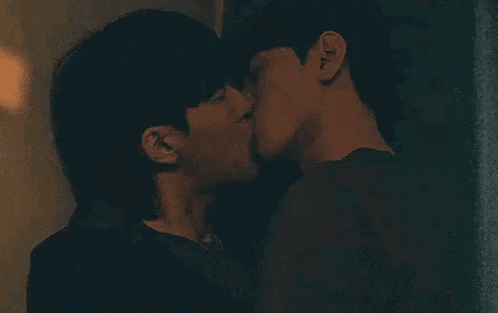 a couple of men are kissing each other on the cheek in a dark room .