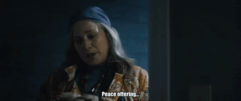 a woman is sitting in a dark room holding a piece of paper and saying peace offering .
