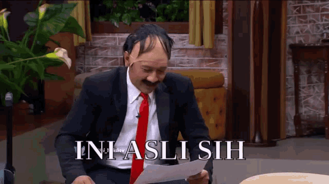 a man in a suit and tie is holding a piece of paper that says " ini asli sih " on it