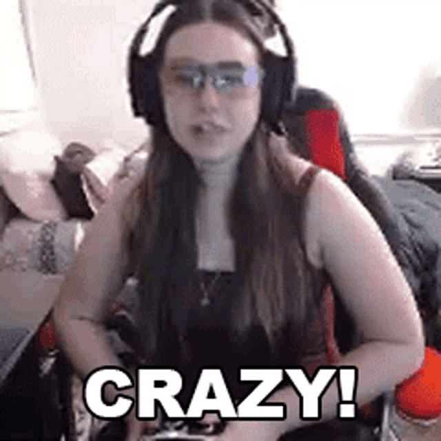 a woman wearing headphones and glasses is sitting in a chair holding a remote control and saying `` crazy ! ''