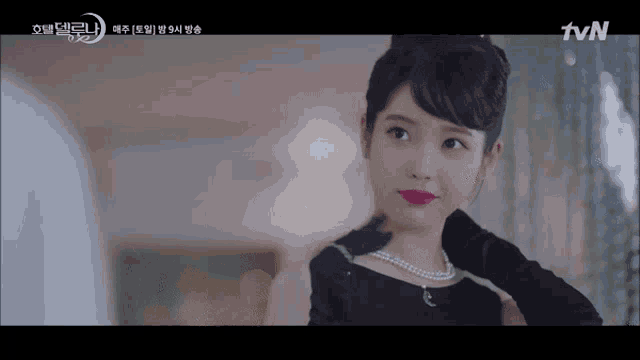 a woman is wearing a black dress and a pearl necklace and is looking at the camera .