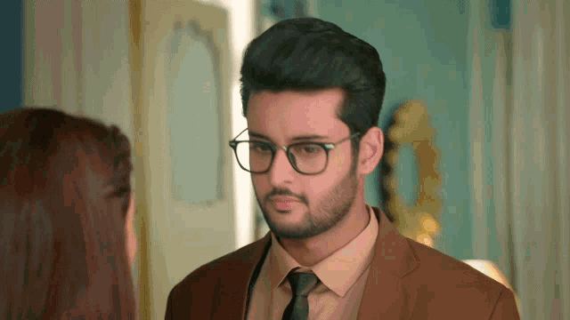 a man wearing glasses and a brown suit looks at a woman