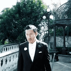 a man in a tuxedo with a flower in his pocket is walking in front of a gazebo
