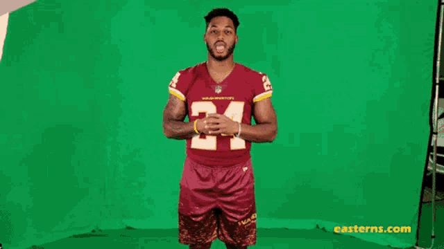 a football player is standing in front of a green screen wearing a red jersey with the number 24 on it .