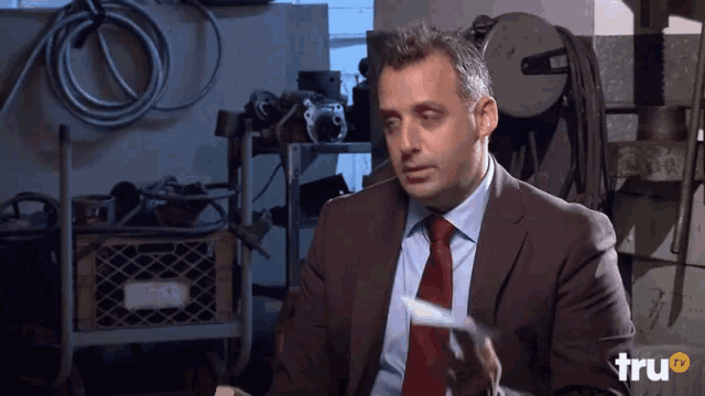 a man in a suit and tie holds a piece of paper in front of a sign that says tru tv