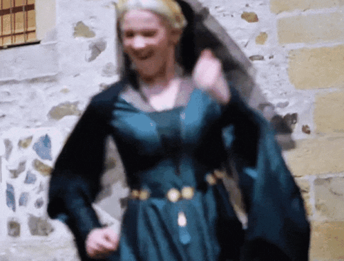 a woman in a blue and black dress is dancing in front of a stone wall
