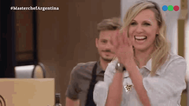 a woman is smiling and clapping in front of a man in an apron on a television show called masterchef argentina .