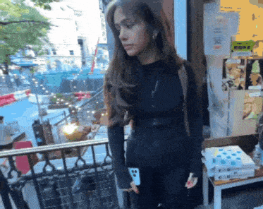 a woman in a black jacket is standing in front of a store with a sign on the wall that says ' a '