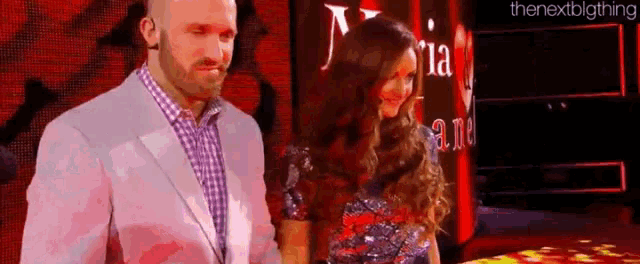 a man in a suit and a woman in a dress are standing next to each other in front of a red wall .