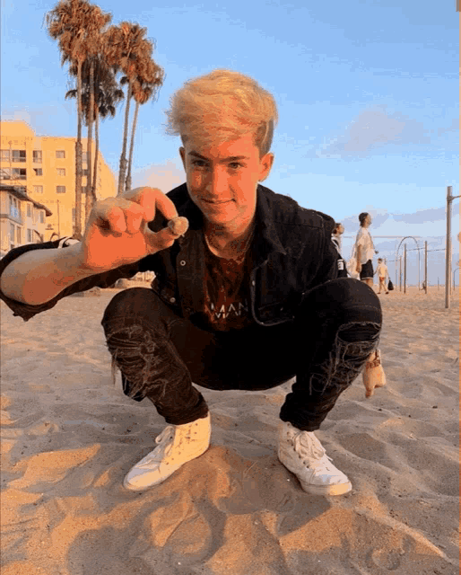 a young man squatting on a beach holding a rock