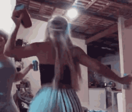 two women are dancing in a room with their arms outstretched and one is holding a can of soda .