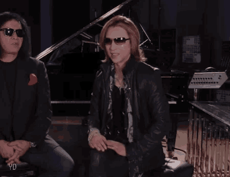 a man wearing sunglasses is sitting next to a man wearing a leather jacket