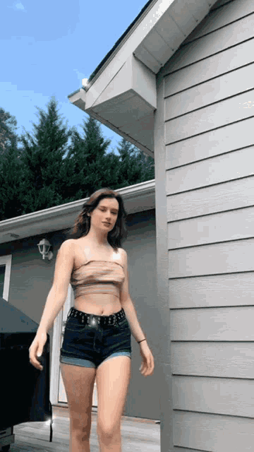 a woman wearing shorts and a crop top stands in front of a house