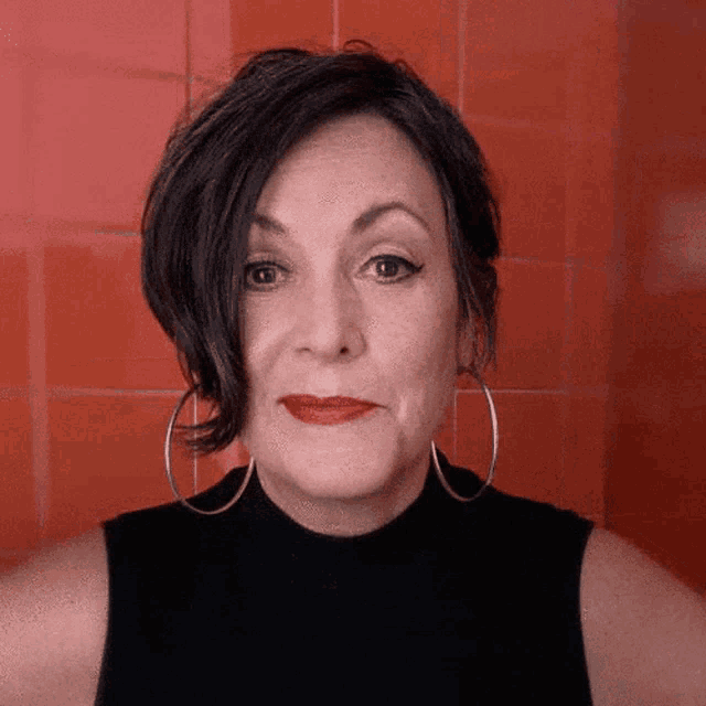 a woman wearing a black top and hoop earrings looks at the camera