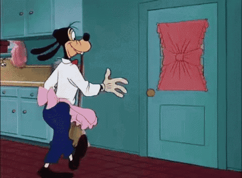 goofy is standing in front of a door in a kitchen .