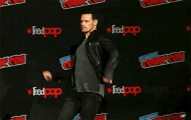 a man in a black jacket is standing in front of a wall that says feedpop