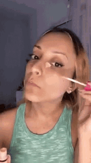 a woman in a green tank top is applying foundation to her face .