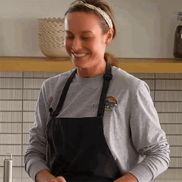 a woman wearing an apron and a gray shirt with a rainbow on it smiles