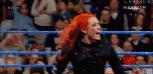 a woman with red hair is standing in a wrestling ring with a crowd behind her .