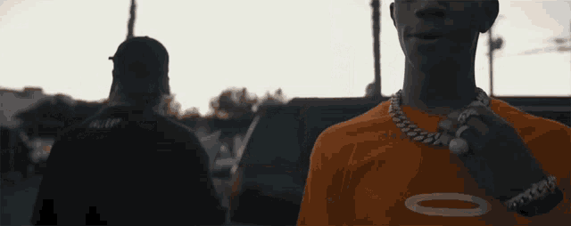 a man wearing an orange t-shirt with a chain around his neck is looking at the camera